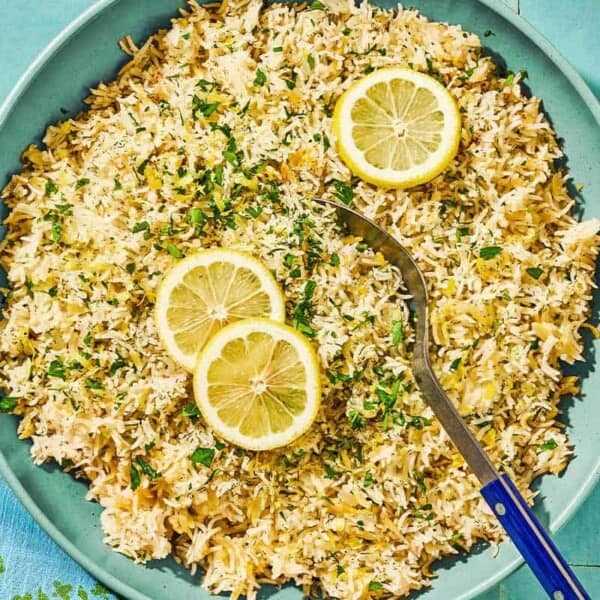 Greek lemon rice topped with lemon wheels in a bowl with a serving spoon.