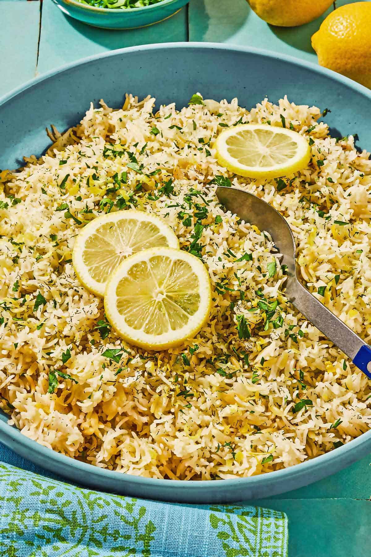 Greek lemon rice topped with lemon wheels in a bowl with a serving spoon.