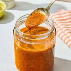 A spoonful of the italian salad dressing being held over the jar with the rest of the dressing.