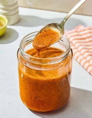 A spoonful of the italian salad dressing being held over the jar with the rest of the dressing.