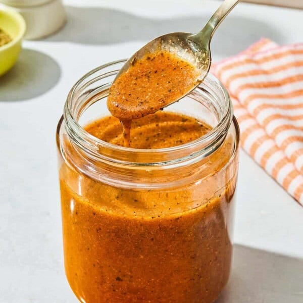 A spoonful of the italian salad dressing being held over the jar with the rest of the dressing.
