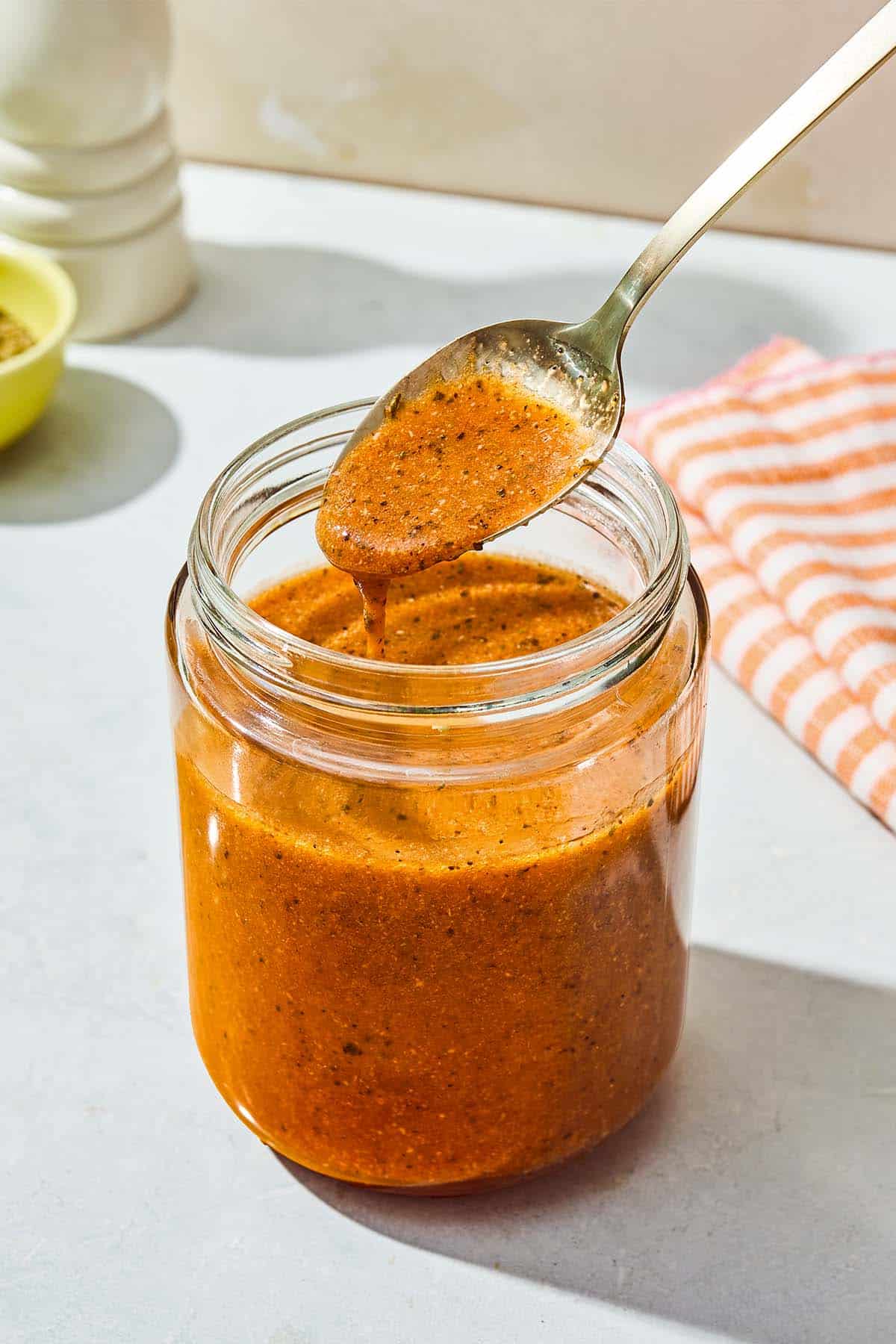 A spoonful of the italian salad dressing being held over the jar with the rest of the dressing.