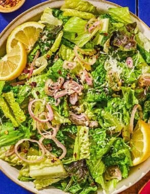 Lemon parmesan lettuce salad in a serving bowl next to a set of wooden serving utensils and a block of parmesan cheese.