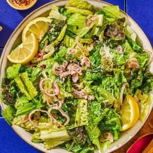 Lemon parmesan lettuce salad in a serving bowl next to a set of wooden serving utensils and a block of parmesan cheese.