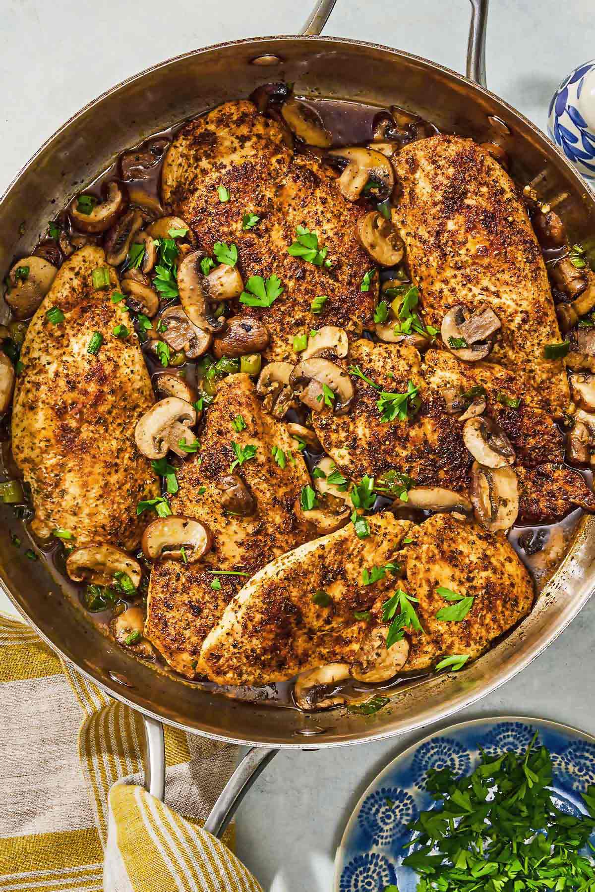 The chicken and mushroom recipe in a skillet next to a bowl of parsley.