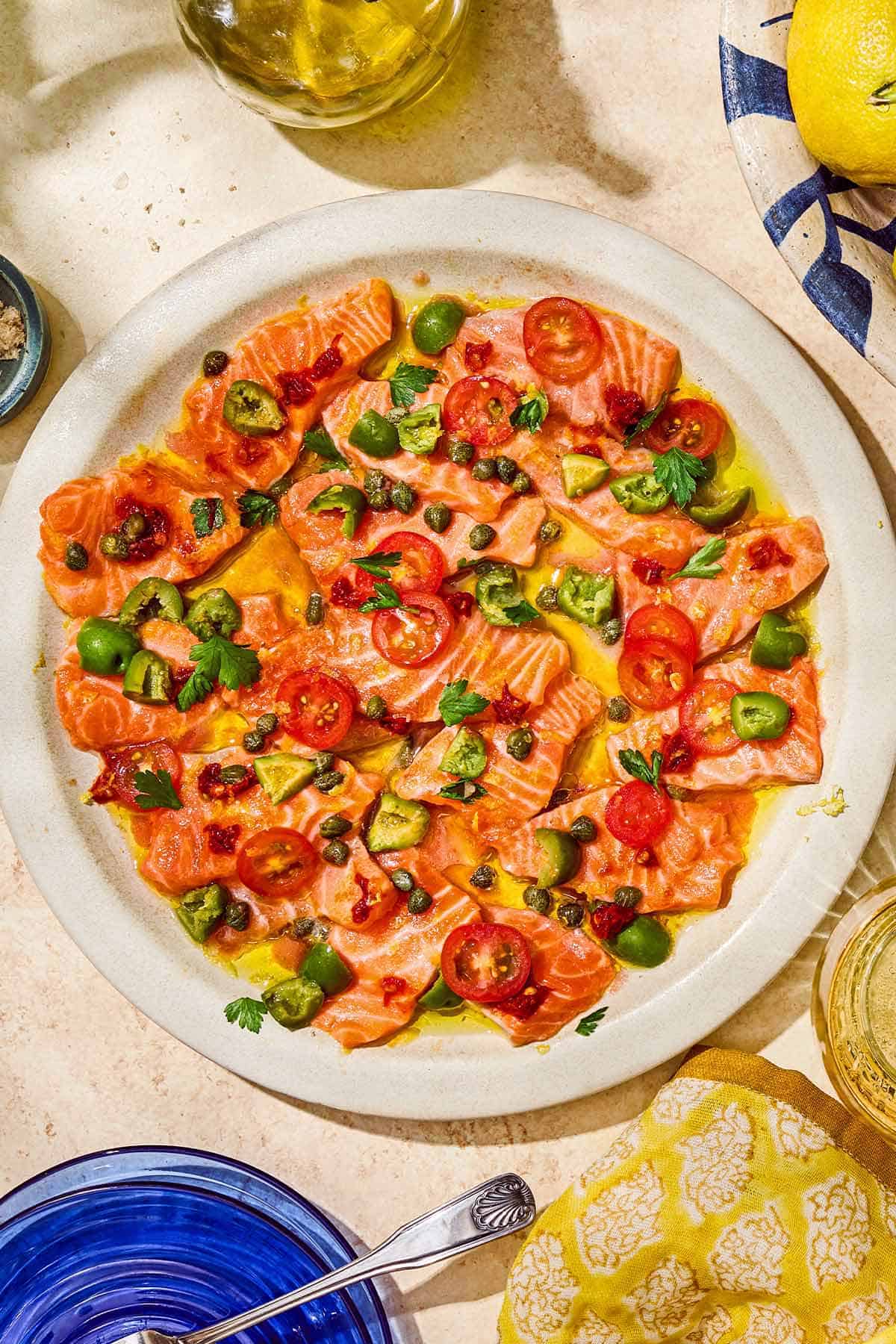 Salmon crudo topped with olives, capers, parsley, chili paste and olive oil on a platter.