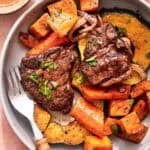 A serving of baked lamb chops with vegetables on a plate with a fork.