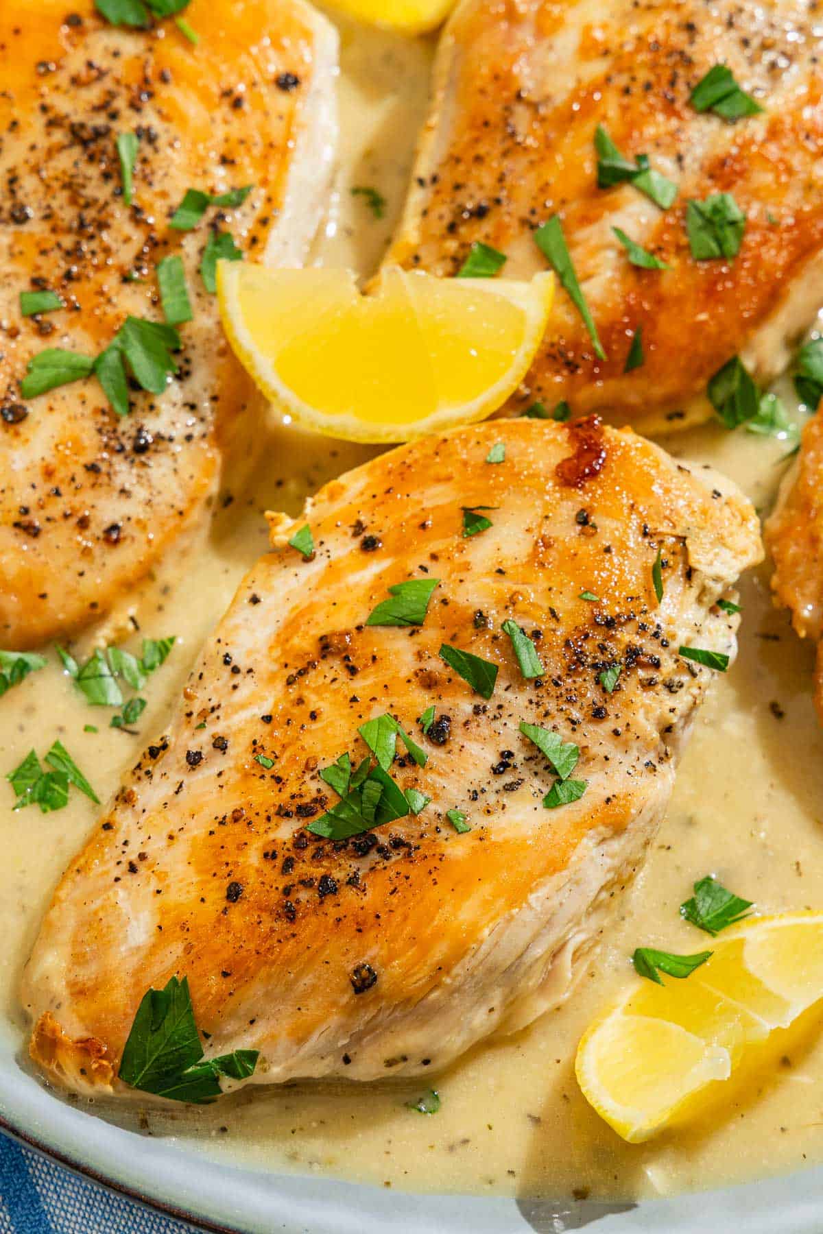 A close up of garlic parmesan chicken topped with sauce and parsley on a plate with lemon wedges.