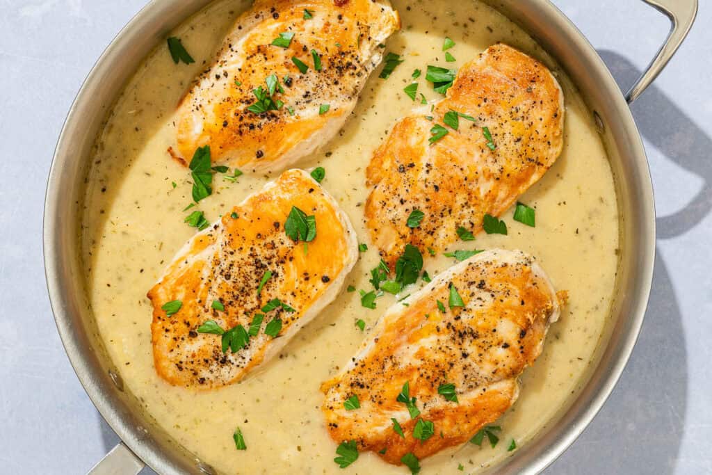 Four garlic parmesan chicken fillets topped with sauce and parsley in a skillet.
