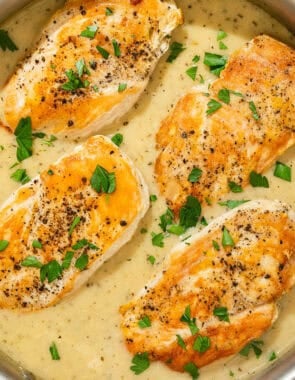 Four garlic parmesan chicken fillets topped with sauce and parsley in a skillet.