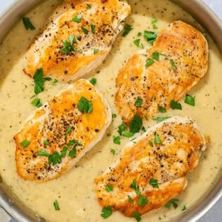 Four garlic parmesan chicken fillets topped with sauce and parsley in a skillet.