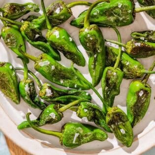 Padron peppers topped with flakey sea salt on a plate.