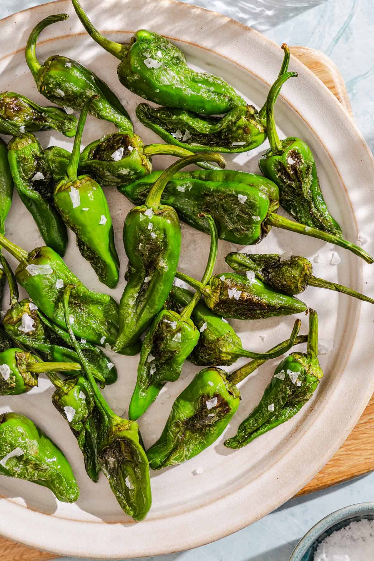 Padron peppers topped with flakey sea salt on a plate.