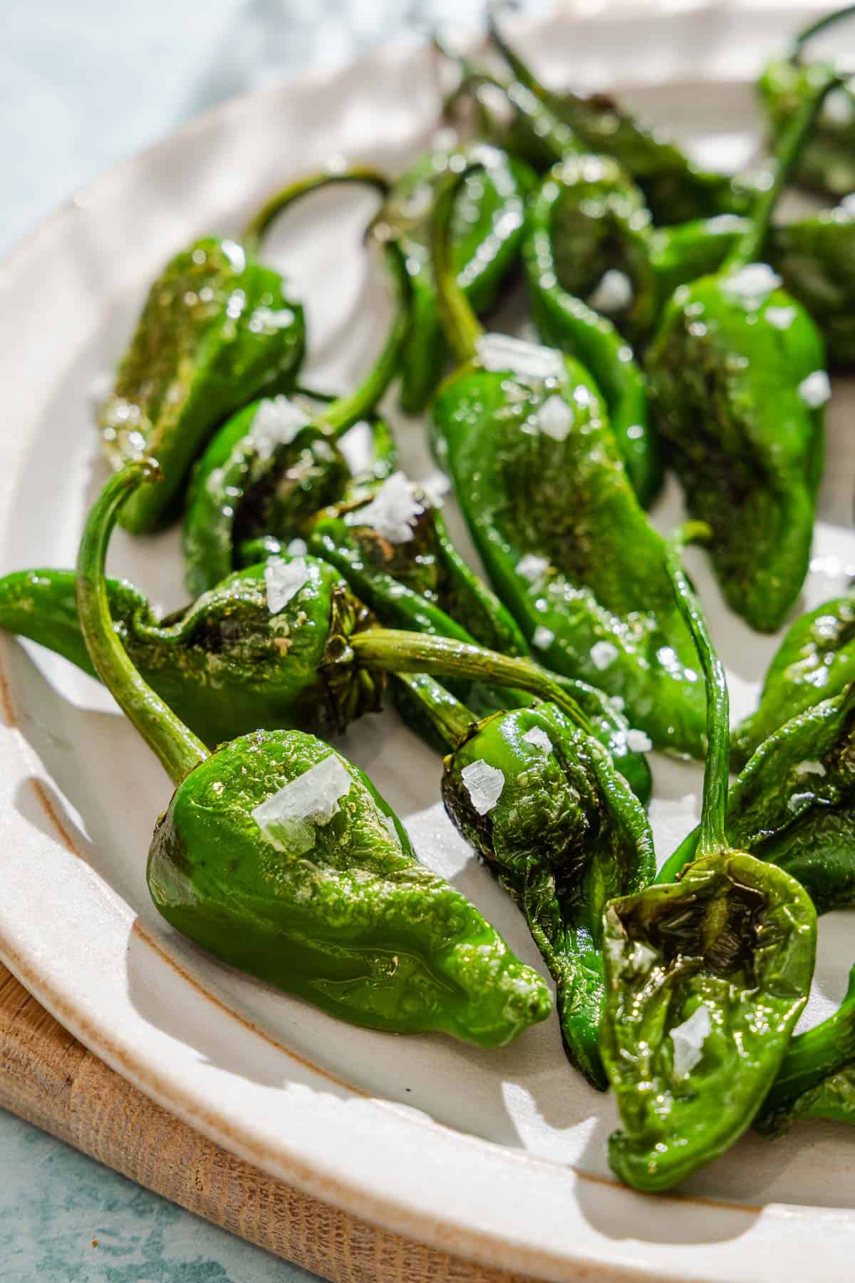 Padron peppers topped with flakey sea salt on a plate.