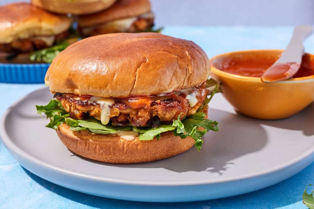 A tuna burger on a plate with bowl of bravas sauce.