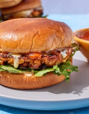 A tuna burger on a plate with bowl of bravas sauce.
