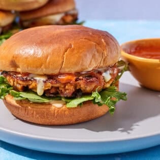 A tuna burger on a plate with bowl of bravas sauce.