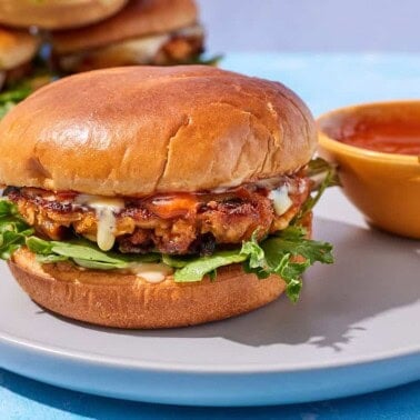 A tuna burger on a plate with bowl of bravas sauce.