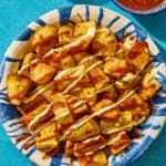 Fried potatoes for the patatas bravas in a serving bowl next to bowls of bravas sauce and aioli.