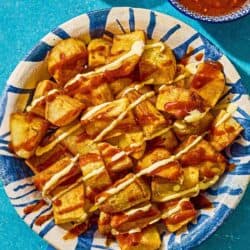 Fried potatoes for the patatas bravas in a serving bowl next to bowls of bravas sauce and aioli.