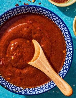 Bravas sauce in a bowl with a wooden spoon next to a small bowl of red pepper flakes.