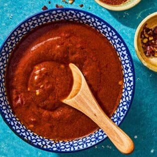 Bravas sauce in a bowl with a wooden spoon next to a small bowl of red pepper flakes.
