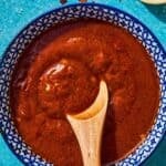 Bravas sauce in a bowl with a wooden spoon next to a small bowl of smoked paprika.