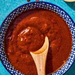 Bravas sauce in a bowl with a wooden spoon next to a small bowl of smoked paprika.