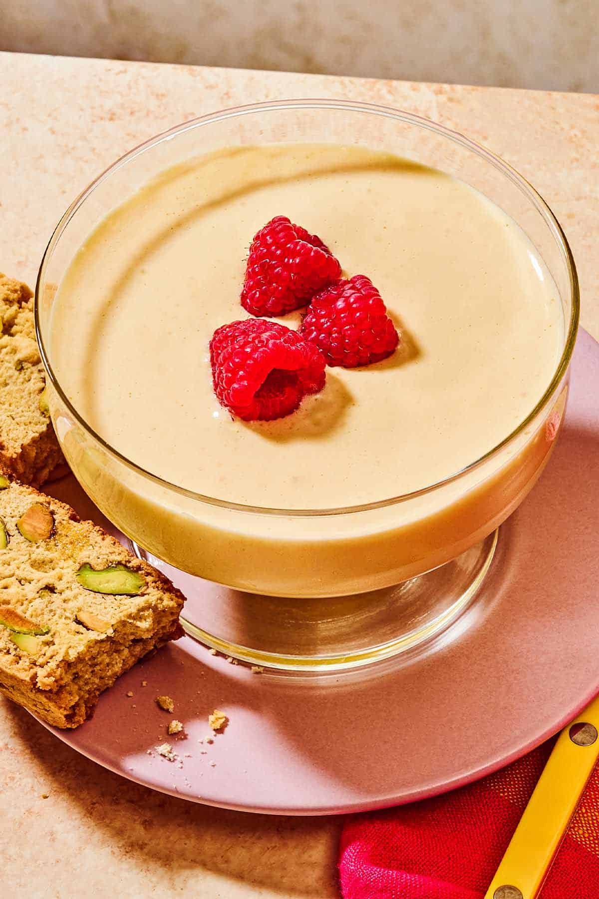 Zabaglione in a bowl topped with raspberries on a plate with biscotti.