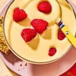 Zabaglione in a bowl topped with raspberries on a plate with biscotti.