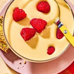 Zabaglione in a bowl topped with raspberries on a plate with biscotti.