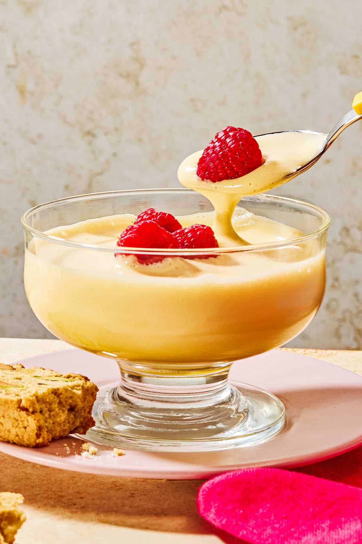 A spoonful of the zabaglione with a raspberry being held over the bowl of zabaglione.