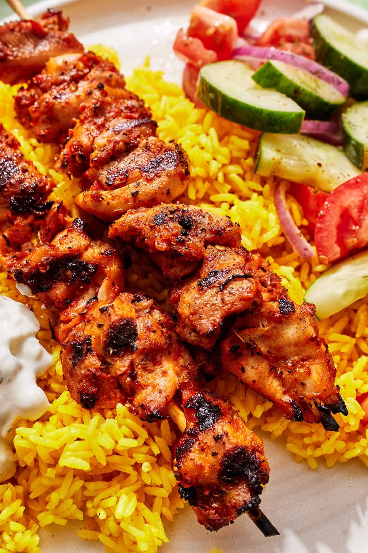 Turkish chicken skewers on a plate with rice, tzatziki and a cucumber and tomato salad.