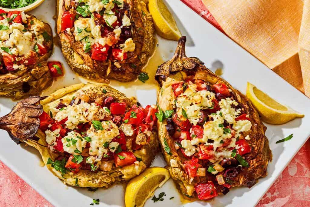 Four grilled eggplant parcels on a platter with lemon wedges.