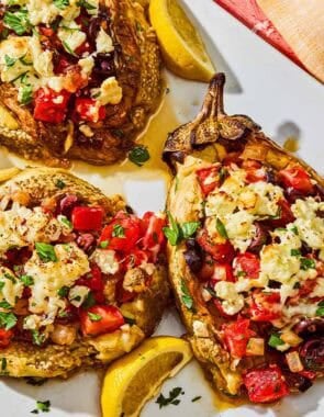 Four grilled eggplant parcels on a platter with lemon wedges.