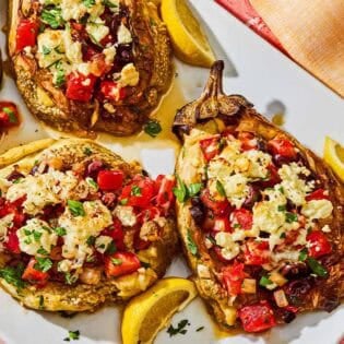 Four grilled eggplant parcels on a platter with lemon wedges.