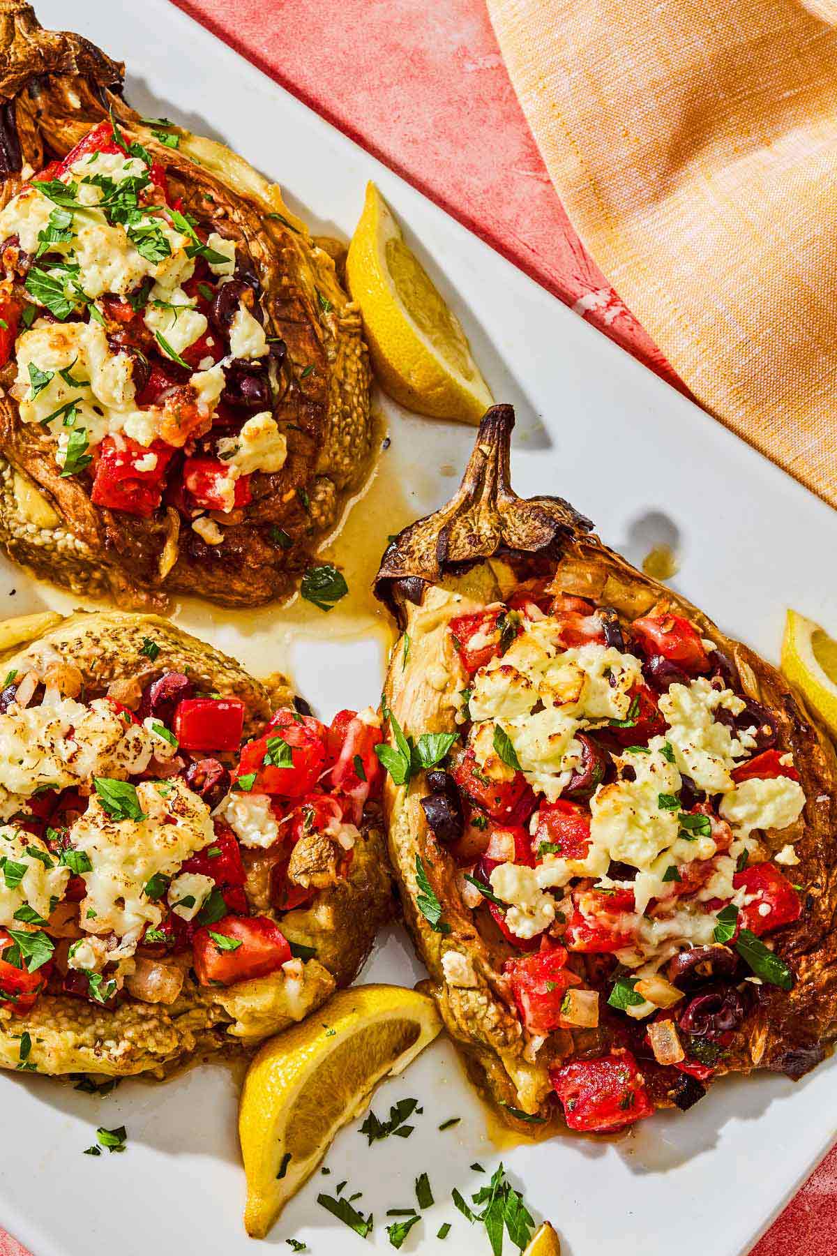 Grilled eggplant parcels on a platter with lemon wedges.