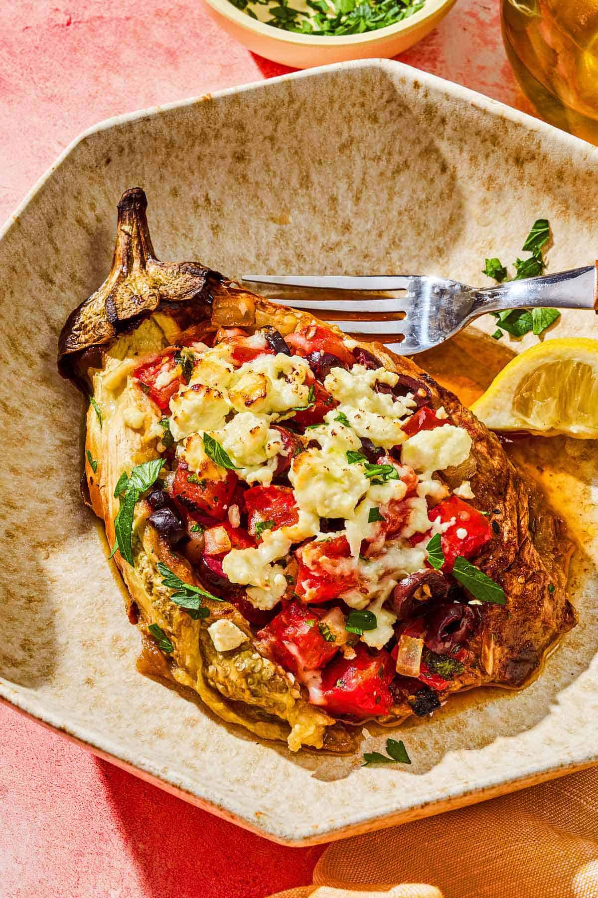 A grilled eggplant parcel on a plate with a fork and a lemon wedge.