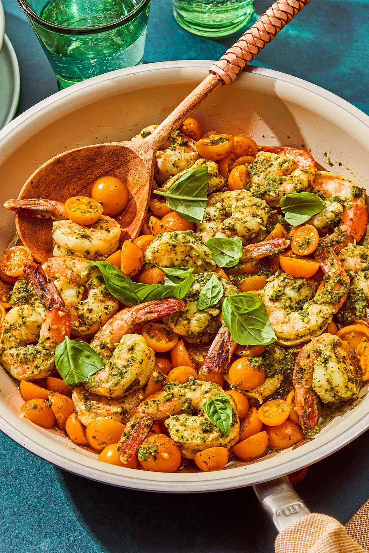 Pesto shrimp in a skillet with a wooden serving spoon.