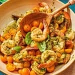 Pesto shrimp in a serving bowl with a wooden serving spoon.