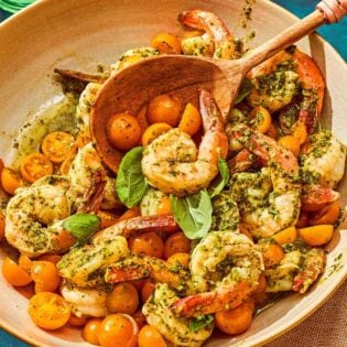 Pesto shrimp in a serving bowl with a wooden serving spoon.