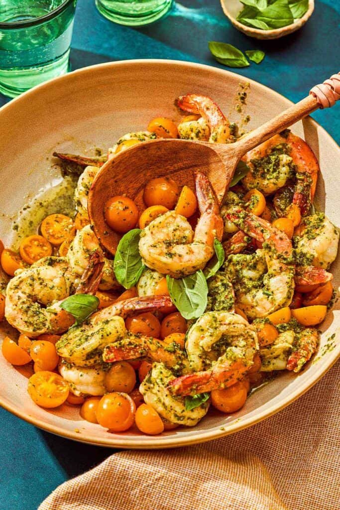 Pesto shrimp in a serving bowl with a wooden serving spoon.