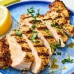 Sliced marinaded chicken on a plate with a lemon wedge.