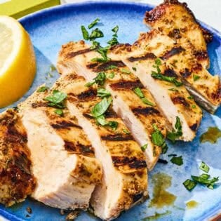 Sliced marinaded chicken on a plate with a lemon wedge.
