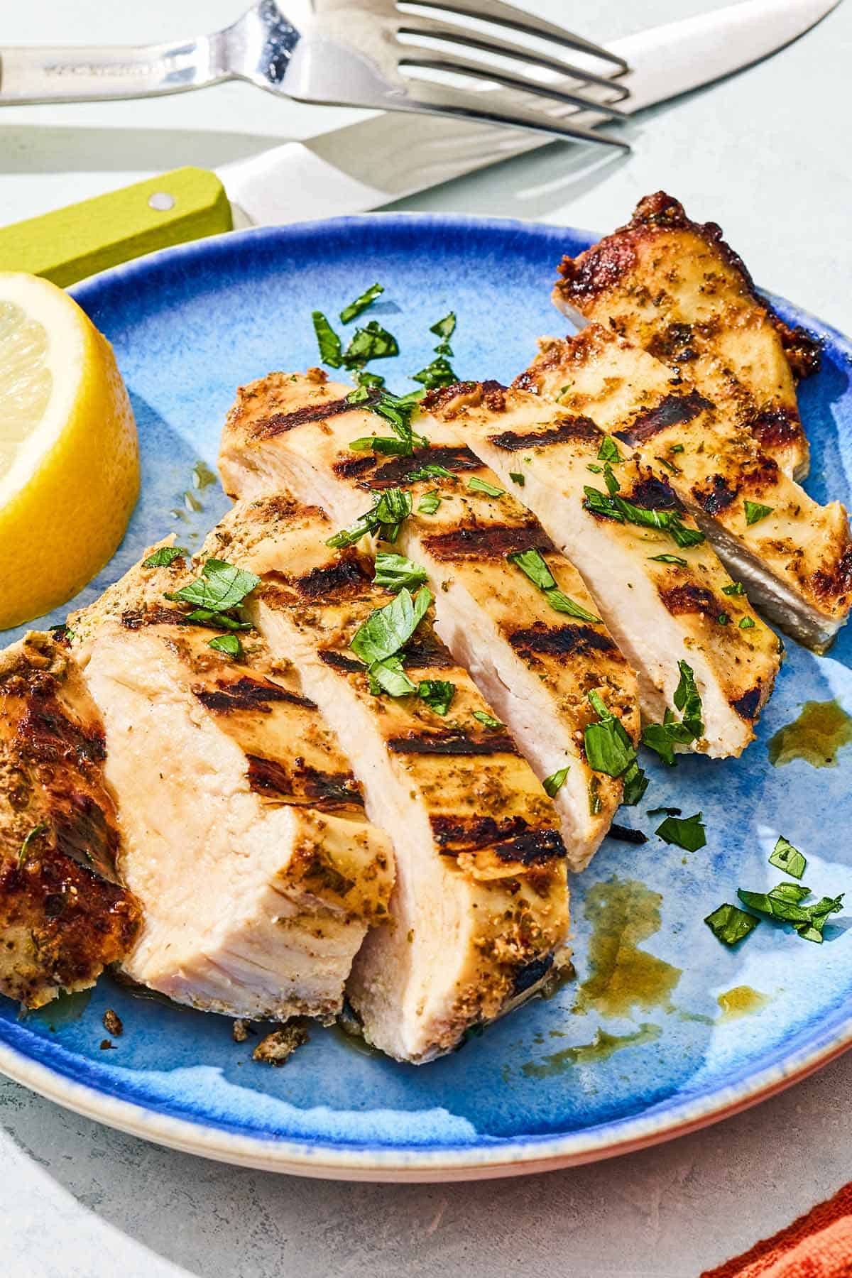 Sliced marinaded chicken on a plate with a lemon wedge.