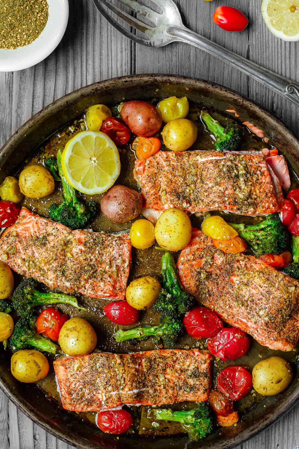 Za'atar salmon in a baking pan next to slotted spoon and a bowl of za'atar.
