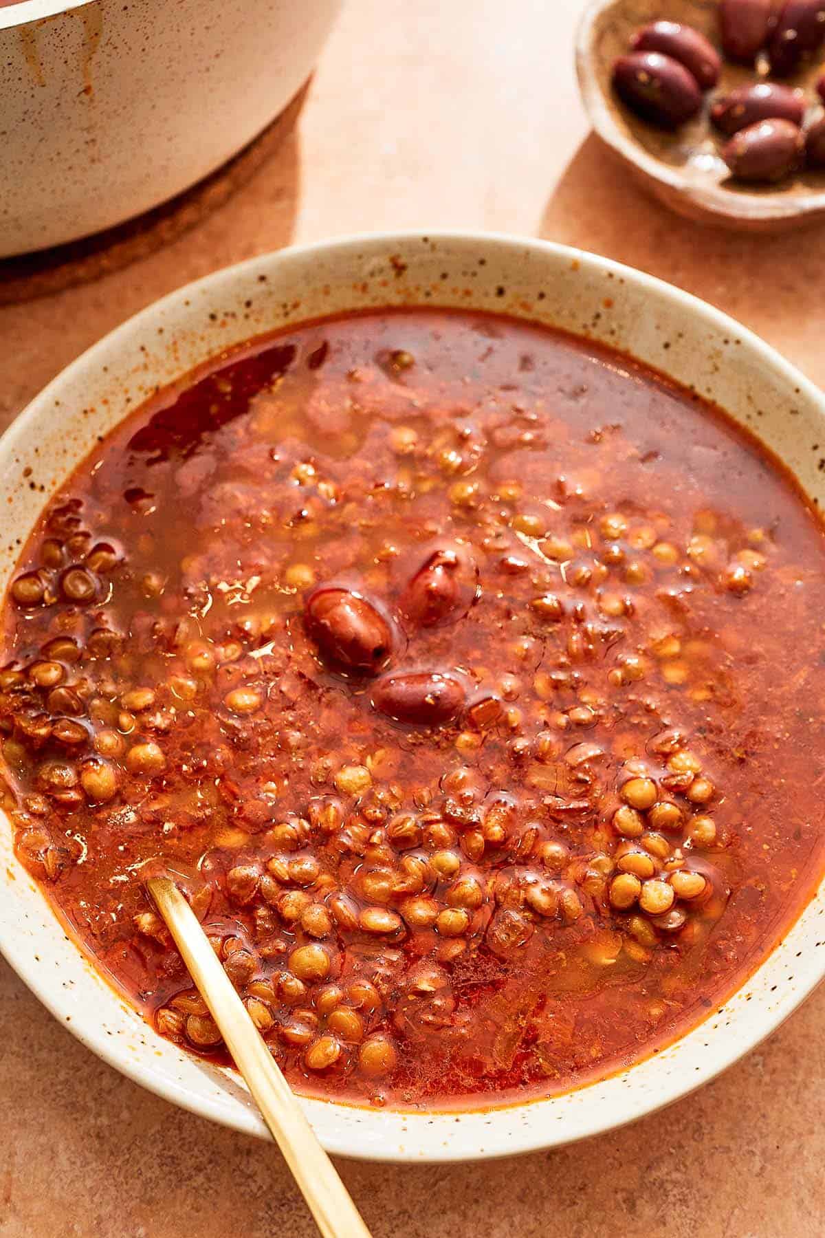 Greek lentil soup in a bowl with a spoon next to a bowl of Kalamata olives.