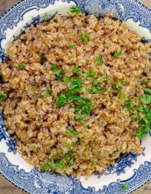 Cooked bulgur in a bowl topped with chopped parsley.