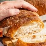 Pan de cristal being sliced on a cutting board.