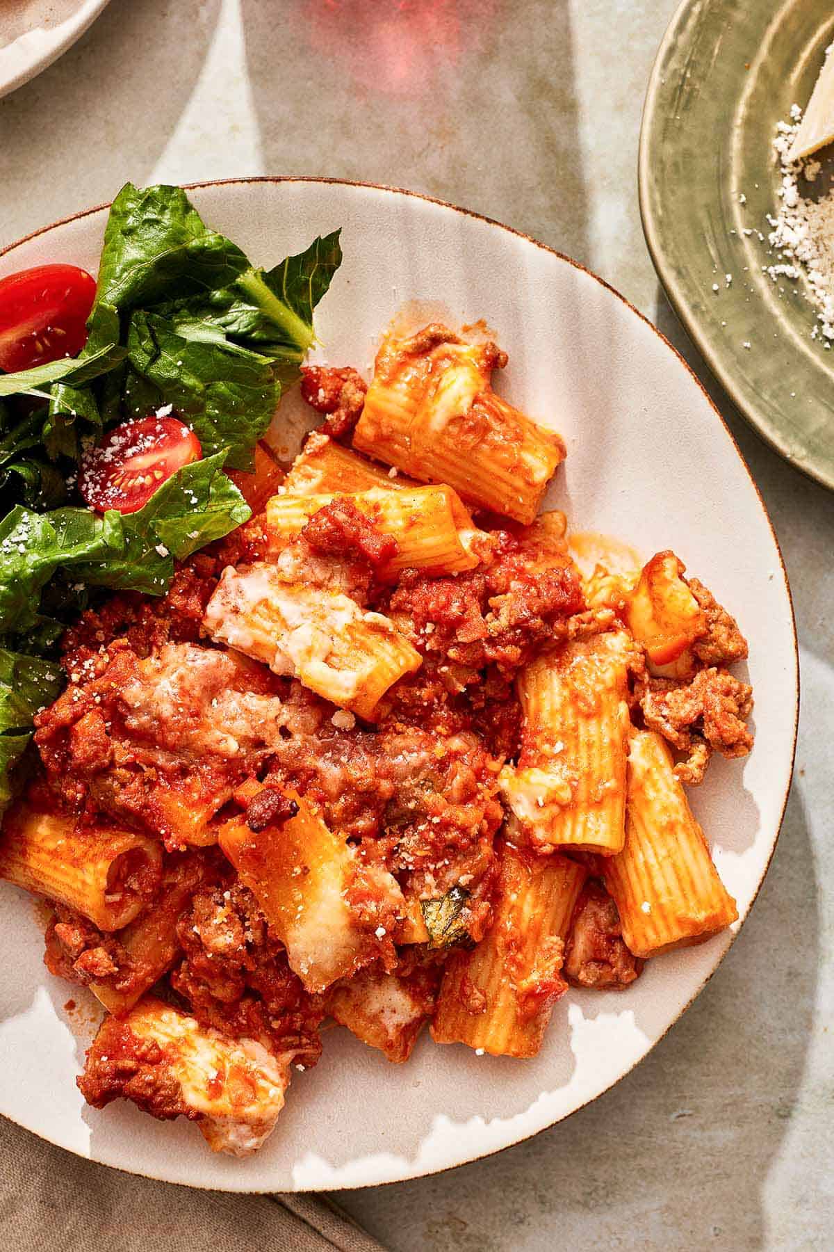 A serving of pasta al forno on a plate with a salad.